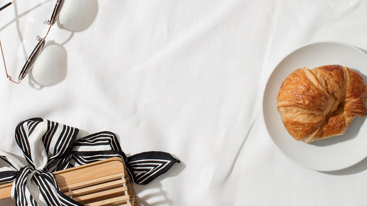 A croissant, pair of sunglasses, and bandana on a white tablecloth