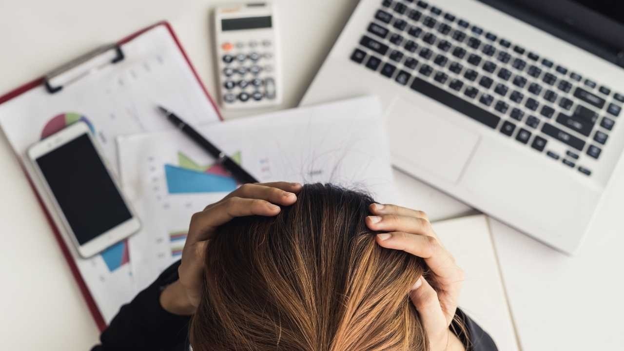 A stressed woman sitting at her workstation, holding her head in her hands